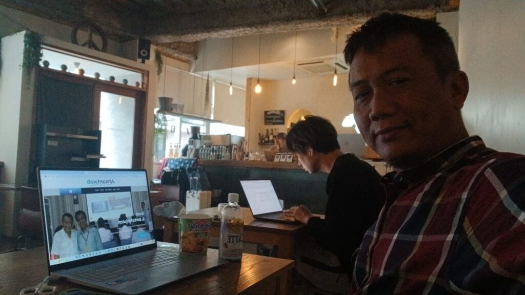 Penulis sedang membuat konten di Almond Cafe & Hostel Tokyo sambil menikmati Pop Mie Sedaap dan coffee latte di meja kerja dengan suasana santai